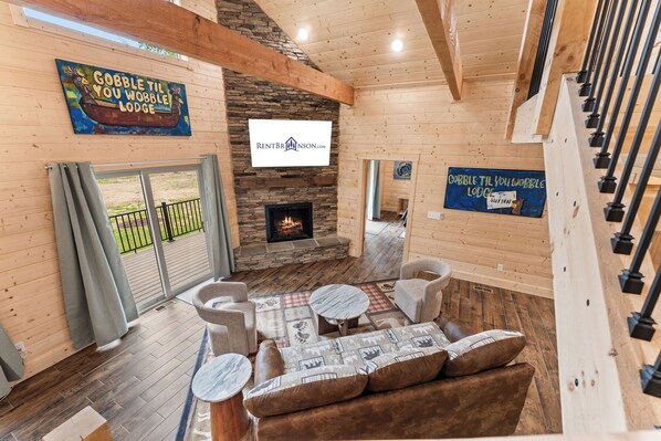 A cozy lodge interior with a stone fireplace, wooden walls, and a dining area with a table and chairs.
