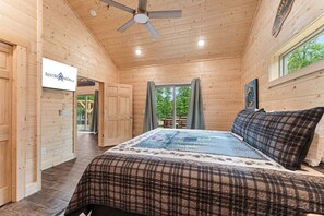 Ein Schlafzimmer in einer Holzhütte mit einem Bett, einem Deckenventilator und einem Fenster.