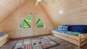 A cozy attic bedroom with a sloped ceiling, two windows, a bed, a sofa, and a patterned rug.
