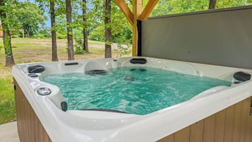 A hot tub with a wooden deck and a view of trees.