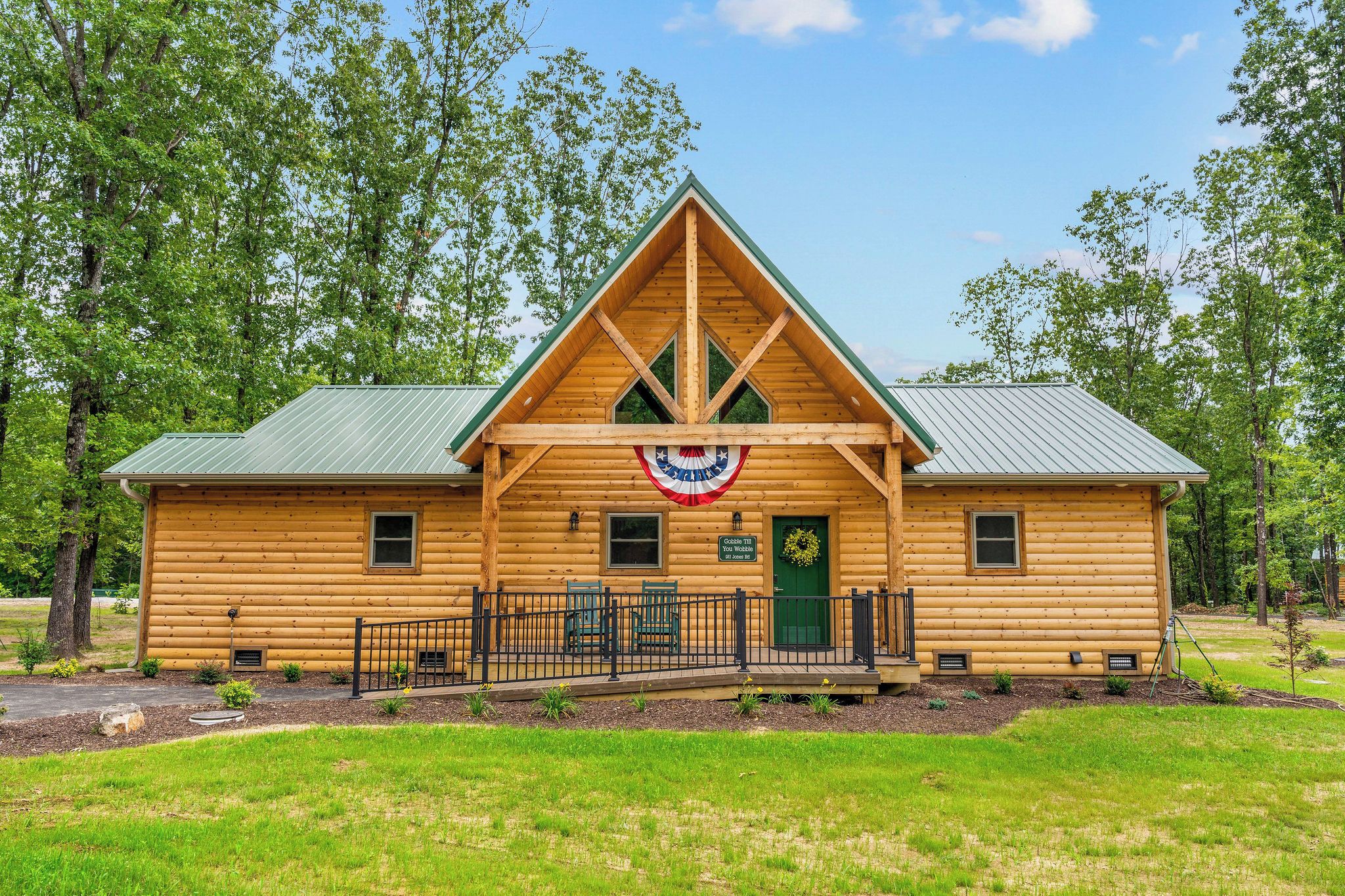 A log cabin with a gabled roof, a porch with chairs, and a flag hanging above the entrance.