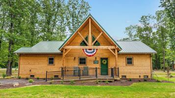 A log cabin with a gabled roof, a porch with chairs, and a flag hanging above the entrance.