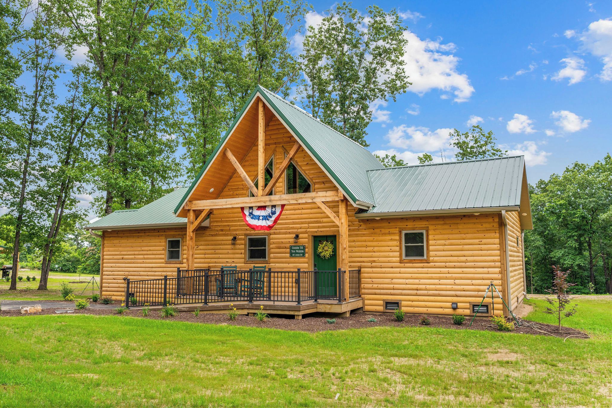 A log cabin with a porch, a flag, and a wreath.