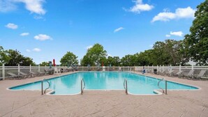 Ein rechteckiger Pool mit einer gefliesten Liegefläche, umgeben von einem weißen Zaun und Bäumen.