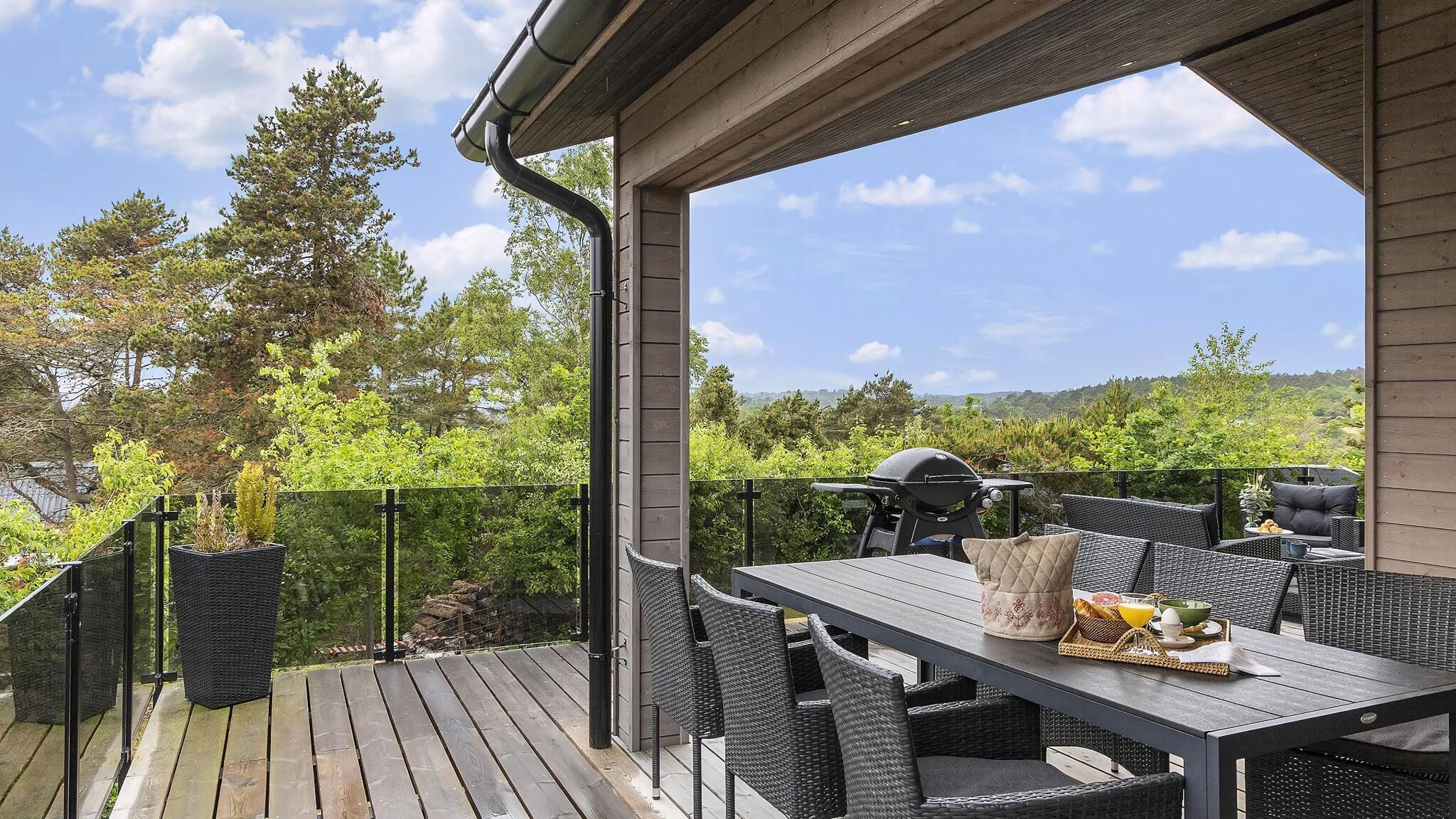 Terraza al aire libre con mesa y sillas, rodeada de follaje y una vista panorámica.