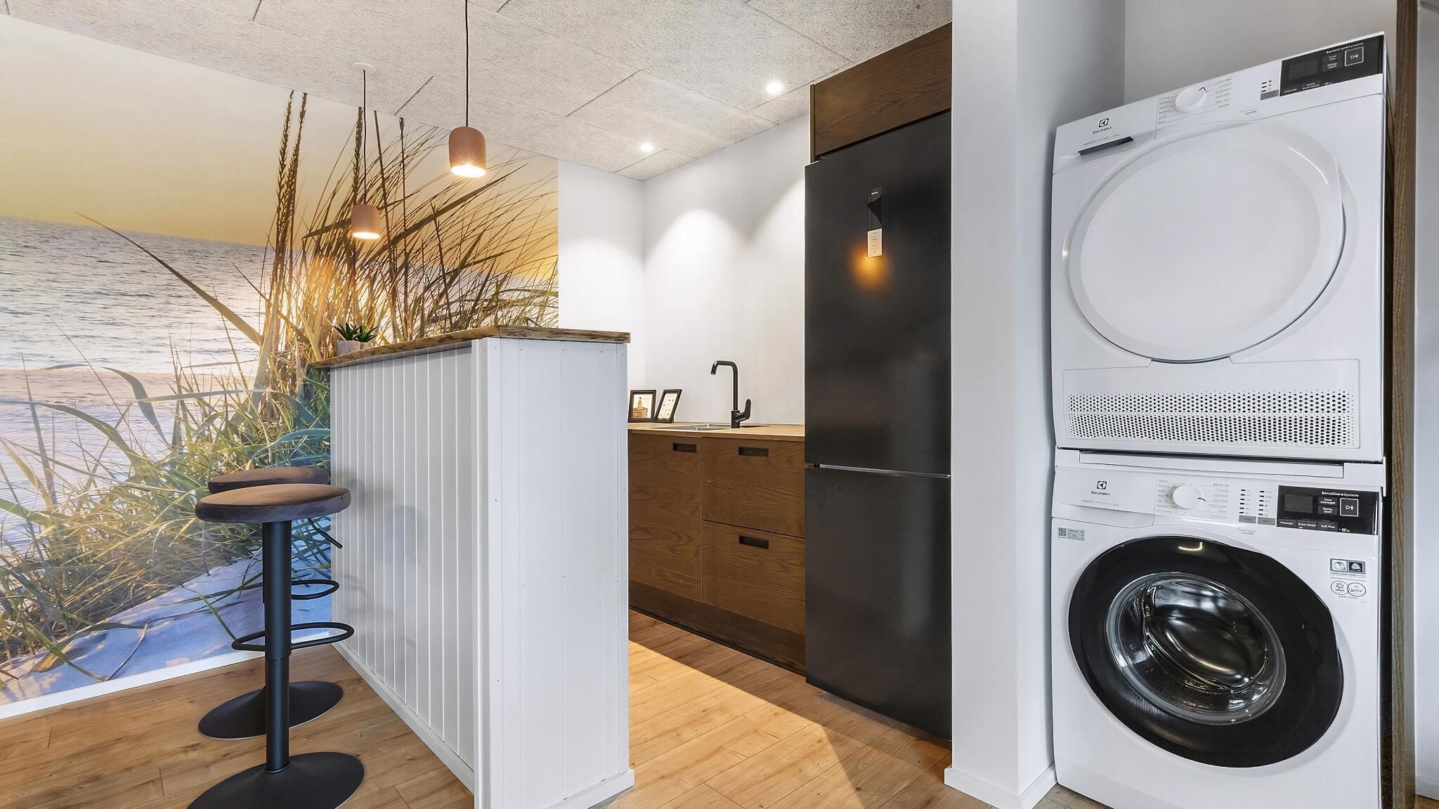 Une cuisine moderne équipée d’un lave-linge et d’un sèche-linge intégrés, de meubles en bois et d’un tabouret de bar.