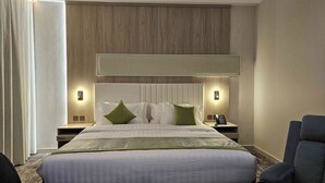 Habitación de hotel con una cama grande, dos mesitas de noche, un cabecero y una lámpara de pared.