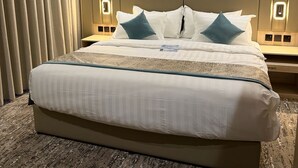 Una habitación de hotel con una cama grande, dos mesitas de noche, un cuadro en la pared y una cortina a la izquierda.