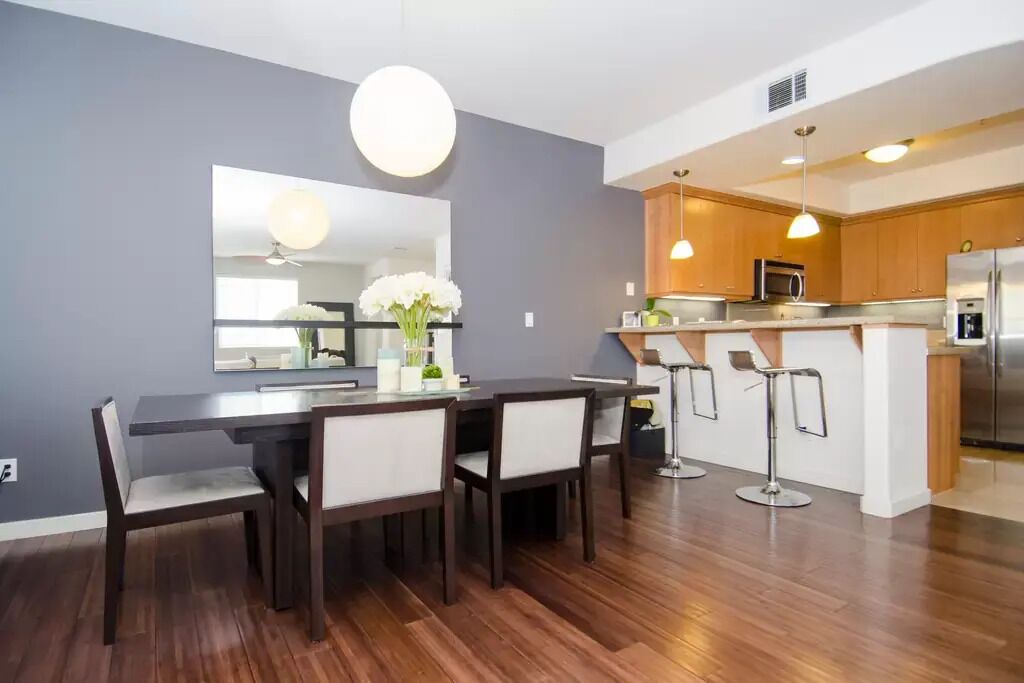 Een moderne keuken met een centraal eiland, barkrukken en een eethoek met een donker houten tafel en stoelen.