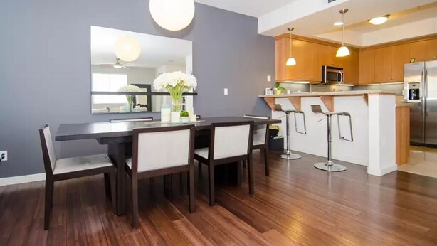 Een moderne keuken met een centraal eiland, barkrukken en een eethoek met een donker houten tafel en stoelen.