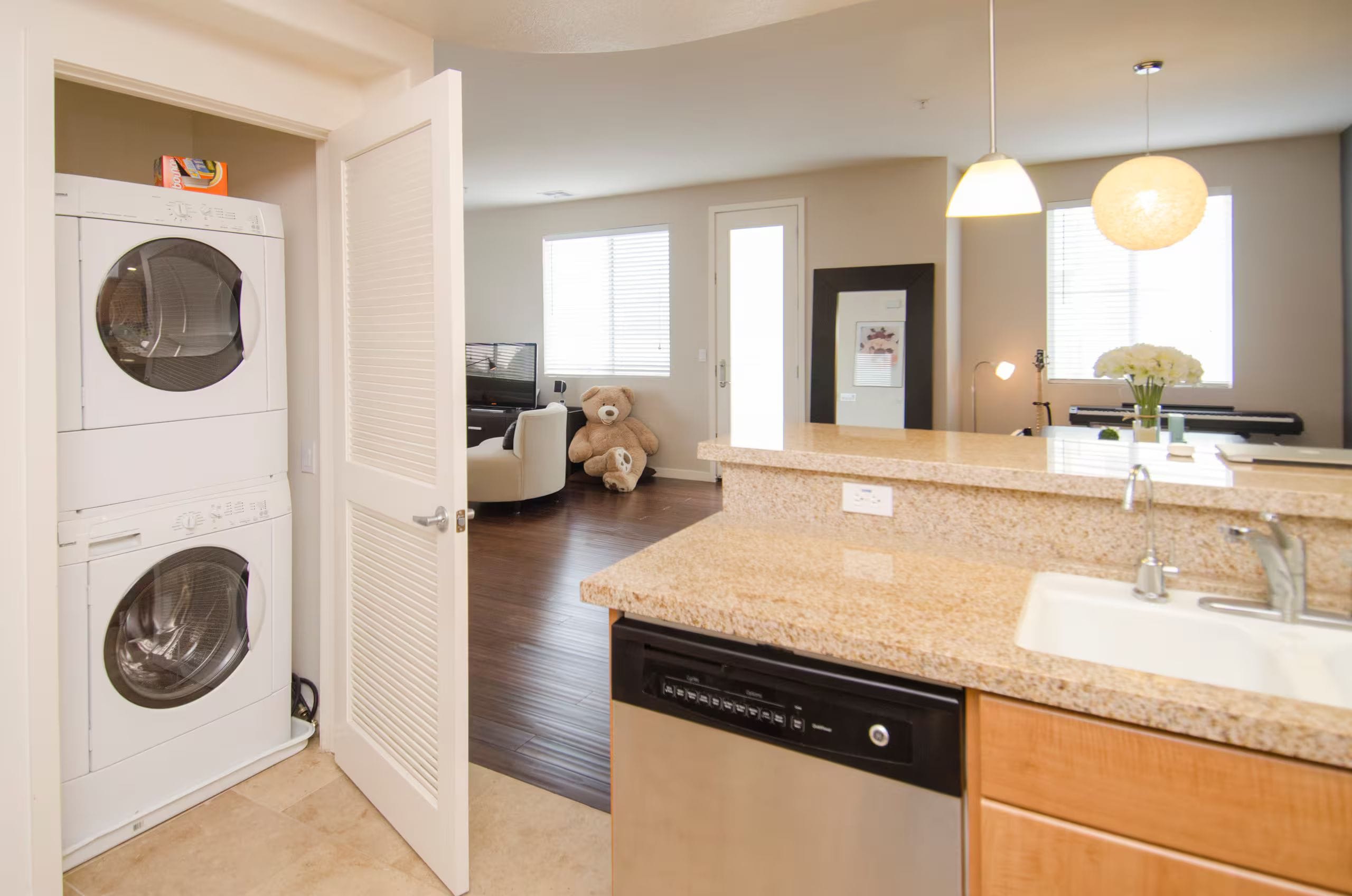A modern kitchen with a dishwasher, a large window, and a dining area with a teddy bear.