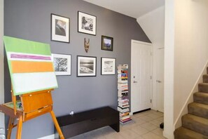 A hallway with a painting on easel, a stack of books, framed pictures on the wall, and a door. - Modern LUXE 2B-2.5B townhome near downtown San Jose with AC and Peloton Bike (San Jose)