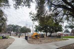 Ein Park mit Spielgeräten, Bänken und einem gepflasterten Weg.