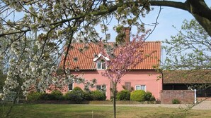 A house with a red roof and pink walls, surrounded by a grassy lawn and trees. - Colston Cottage, Badingham (Badingham)