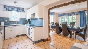 A kitchen with white cabinets, a blue countertop, and a dining area with a table and chairs. - Colston Cottage, Badingham (Badingham)
