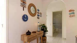 Un pasillo con una consola de madera, un espejo, relojes de pared y una planta en maceta.