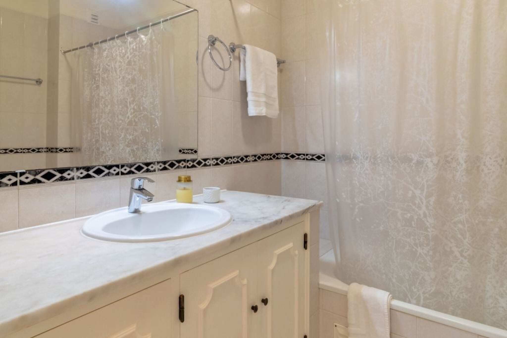 Un baño con lavamanos, espejo, toallero y cortina de ducha.