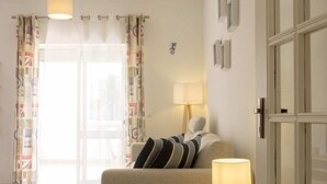 Un dormitorio con cama, mesita de noche con lámpara, puerta con paneles de vidrio y vistas al exterior a través de una ventana con cortinas.