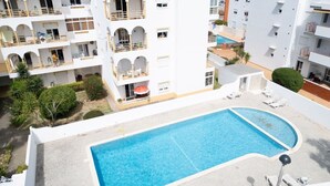 Un área de piscina con una pileta rectangular, sillones de descanso y un edificio con balcones.