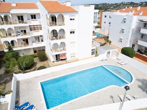 Ein Poolbereich mit rechteckigem Pool, Liegestühlen und einem Gebäude mit Balkonen.