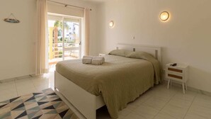 Un dormitorio con una cama, una mesita de noche, una lámpara en la pared y vistas a través de una puerta.