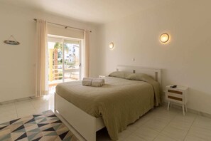 Ein Schlafzimmer mit Bett, Nachttisch, Wandlampe und Blick durch eine Tür.