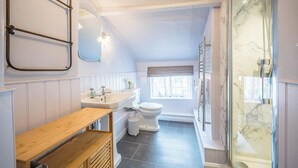 A bathroom with a wooden bench, a sink, a toilet, and a shower area. - Barnaby Cottage, Southwold (Southwold)
