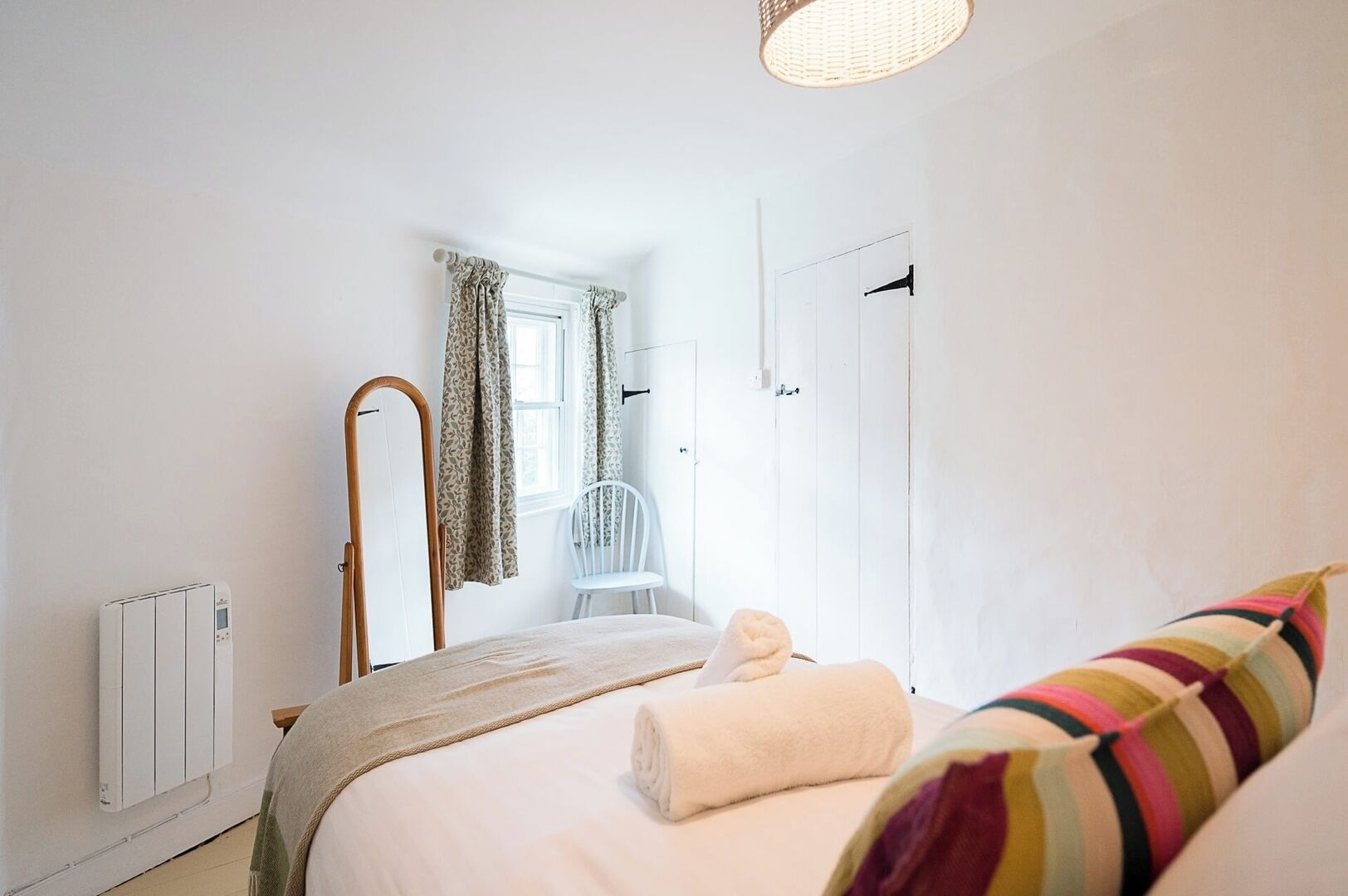 A bedroom with a bed, a chair, a radiator, a mirror, and a window with curtains.