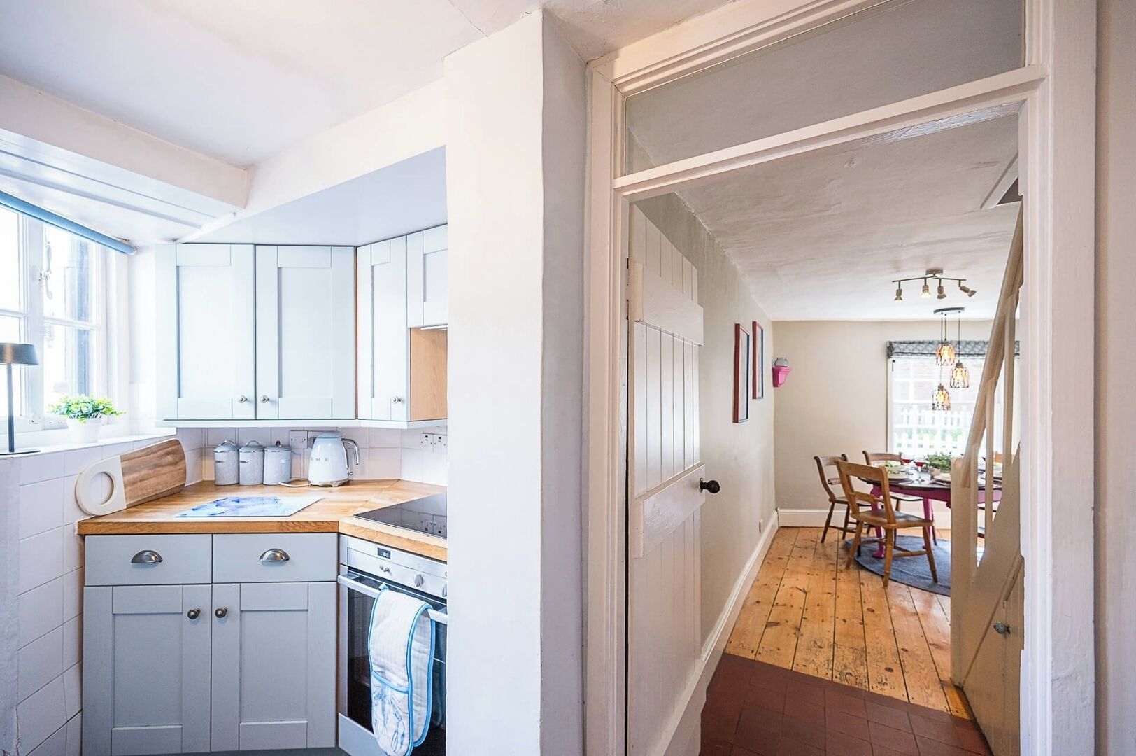 Una cocina con armarios blancos, encimera de madera y estufa. Se ve un comedor con una mesa y sillas a través de un ventanal.