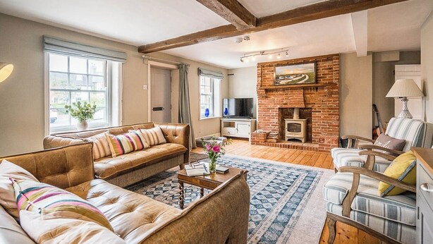 A living room with a fireplace, leather sofas, a television, and a wooden floor. - Barnaby Cottage, Southwold (Southwold)