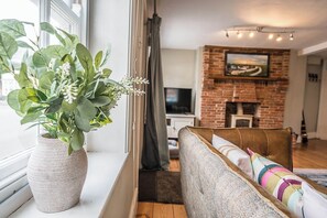 Ein Wohnzimmer mit Sofa, Fernseher, Kamin und einem Fenster mit Pflanze.