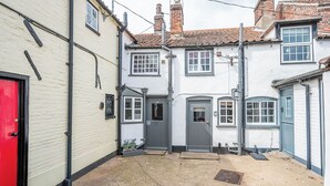 A narrow alleyway with a red door, a grey door, and a white building with a blue window. - Barnaby Cottage, Southwold (Southwold)