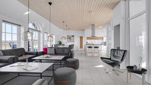 Un espacio moderno para la vida con un sofá, una mesa de centro, un reposapiés y un sillón de cuero negro. Hay una zona de cocina con una barra y taburetes.