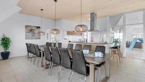 A modern kitchen with a central island, pendant lighting, and a dining area with a long table and chairs. - VillaVilla 982 - Vedersø Klit, Vestjylland (Ulfborg)