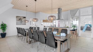 Cocina moderna con una isla central, iluminación colgante y una zona de comedor con una mesa larga y sillas.