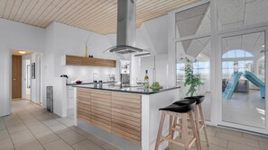 A modern kitchen with a central island, wooden cabinetry, and a large window offering a view of the outside. - VillaVilla 982 - Vedersø Klit, Vestjylland (Ulfborg)