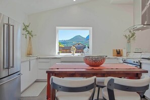 A modern kitchen with a wooden table, two chairs, a large bowl, and a view of a mountain landscape through a window. - Kenwood Wine Country Cottage (Kenwood)
