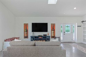A living room with a flat-screen TV, a fireplace, and a door leading to a garage. - Kenwood Wine Country Cottage (Kenwood)