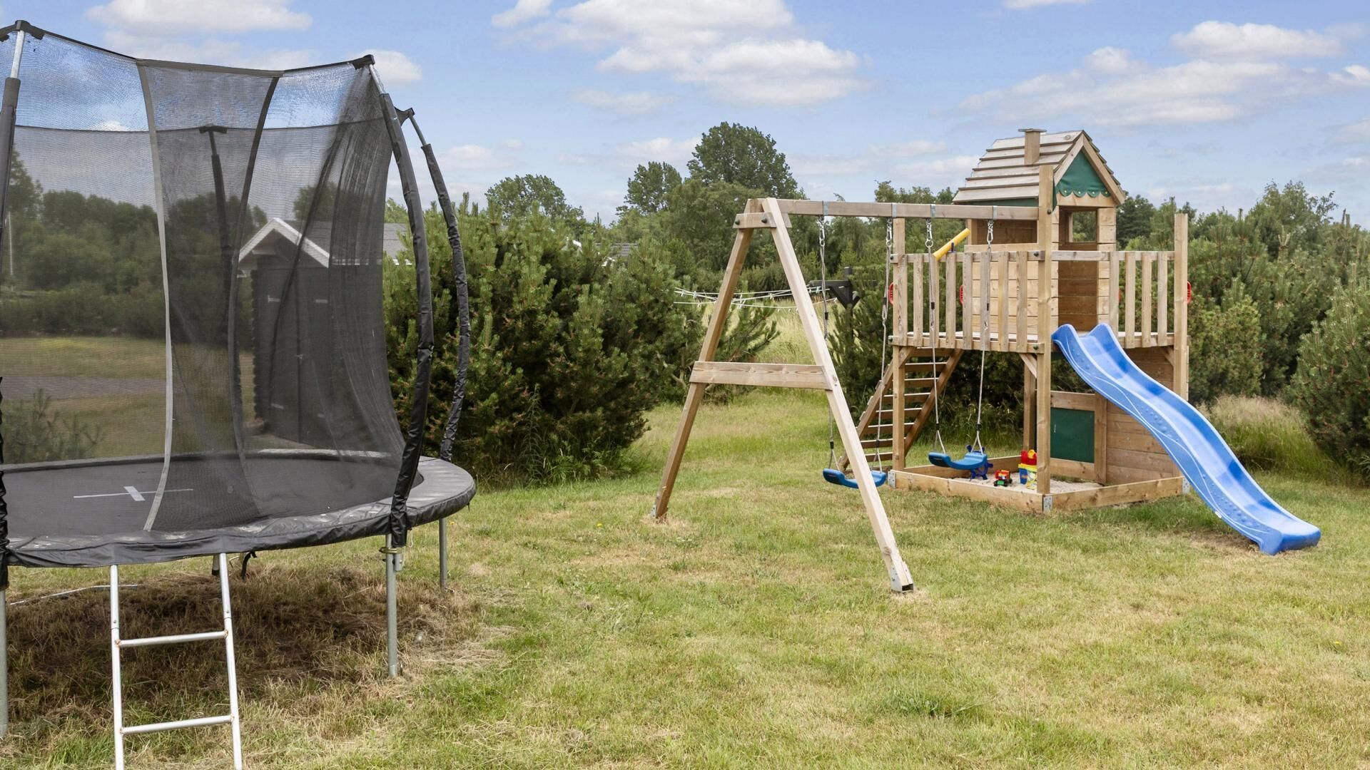 Un trampoline, une balançoire en bois et une cabane de jeux avec un toboggan, le tout installé dans un espace extérieur verdoyant.