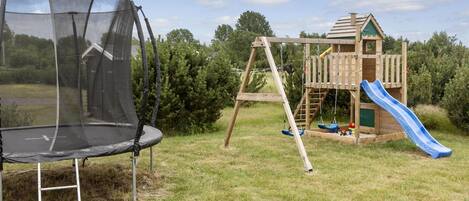 Un trampolín, un conjunto de columpios de madera y una casita de juegos con tobogán en un área verde al aire libre.