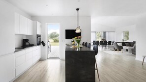 Eine moderne Küche mit weißen Schränken, einer schwarzen Arbeitsplatte und einer großen Kochinsel. Ein Essbereich mit Tisch und Stühlen lädt zum Verweilen ein, und ein Wohnzimmer bietet eine Couch und einen Fernseher.