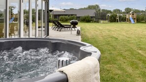 Ein Whirlpool mit Blick auf eine Terrasse und einen Spielbereich im Freien.