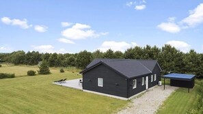 Ein einstöckiges Gebäude mit dunklem Dach, einer überdachten Außenlounge und einer Solaranlage.