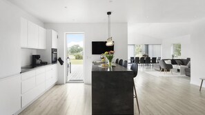 Une cuisine moderne avec un îlot central, un coin repas avec une longue table et un espace de vie comprenant un canapé et un téléviseur.