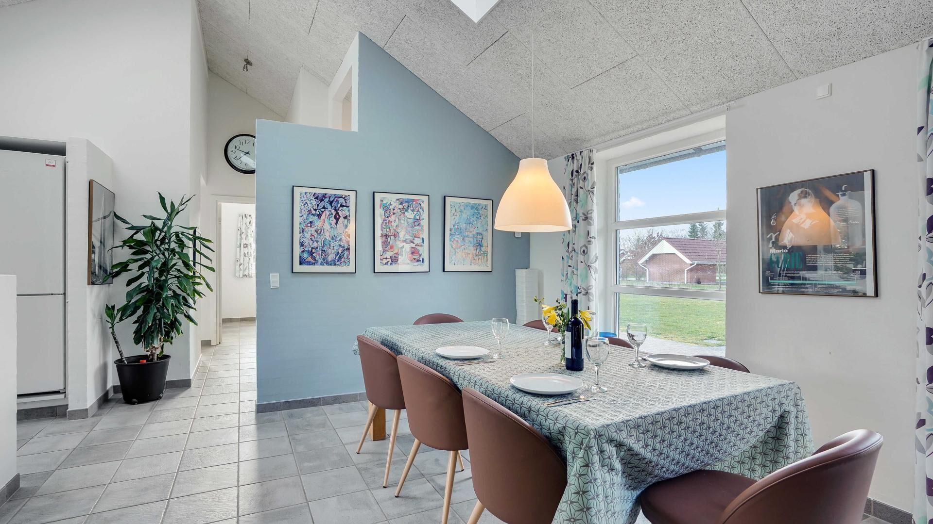 A dining area with a table set for two, a potted plant, and framed artwork on the wall.