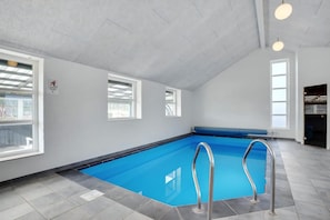 Een binnenzwembad met een blauw waterkunstwerk, een metalen zwemplatform en een plafond met zichtbare balken.