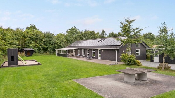 A modern house with a large patio area, outdoor seating, and a small play structure.