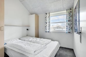 Een slaapkamer met een bed, een raam met gordijnen, een deur en een lichtschakelaar aan de muur.