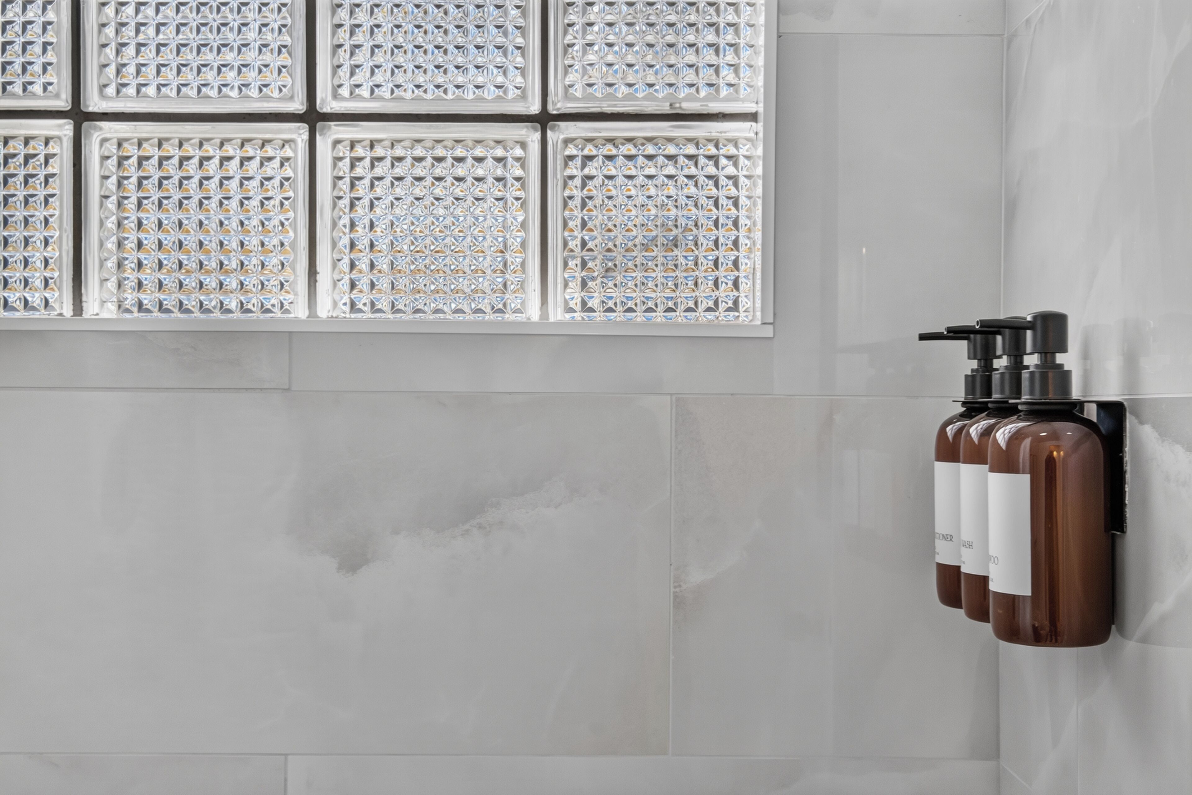 Ein Badezimmer mit gefliesten Wänden, einem Fenster mit geometrischem Muster und einem Wandspender.