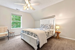 Ein Schlafzimmer mit Bett, Sessel, Fenster, Deckenventilator und Nachttisch.
